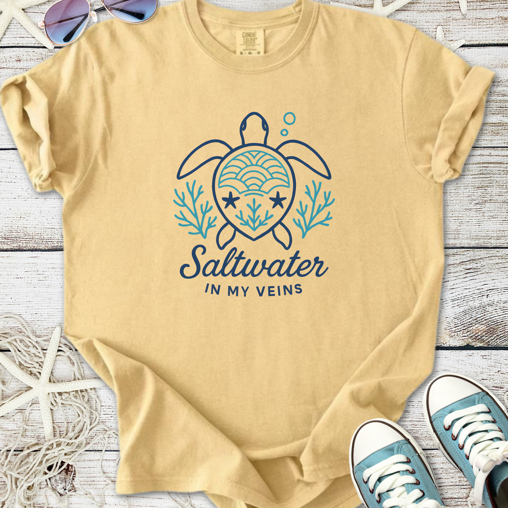 Tan t-shirt with turtle graphic and "Saltwater in My Veins" text, perfect for beach lovers.