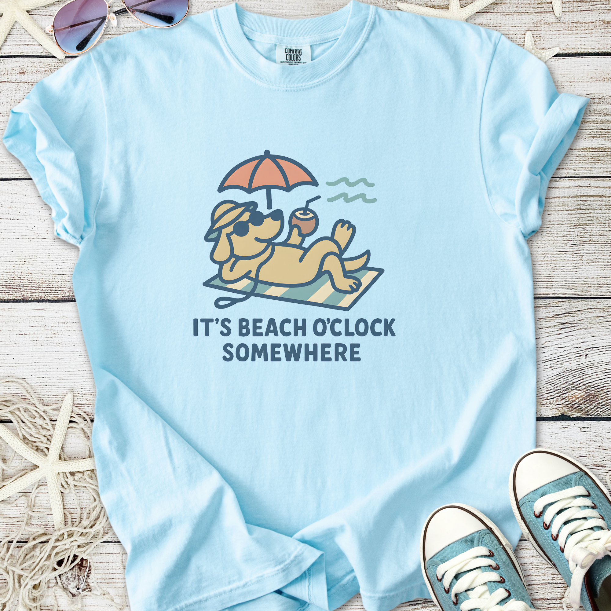 Light blue t-shirt featuring a dog relaxing under an umbrella with text 'It's Beach O'Clock Somewhere'