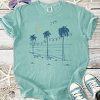 Mint green graphic t-shirt featuring beach scene with palm trees and chairs, perfect for casual summer wear.