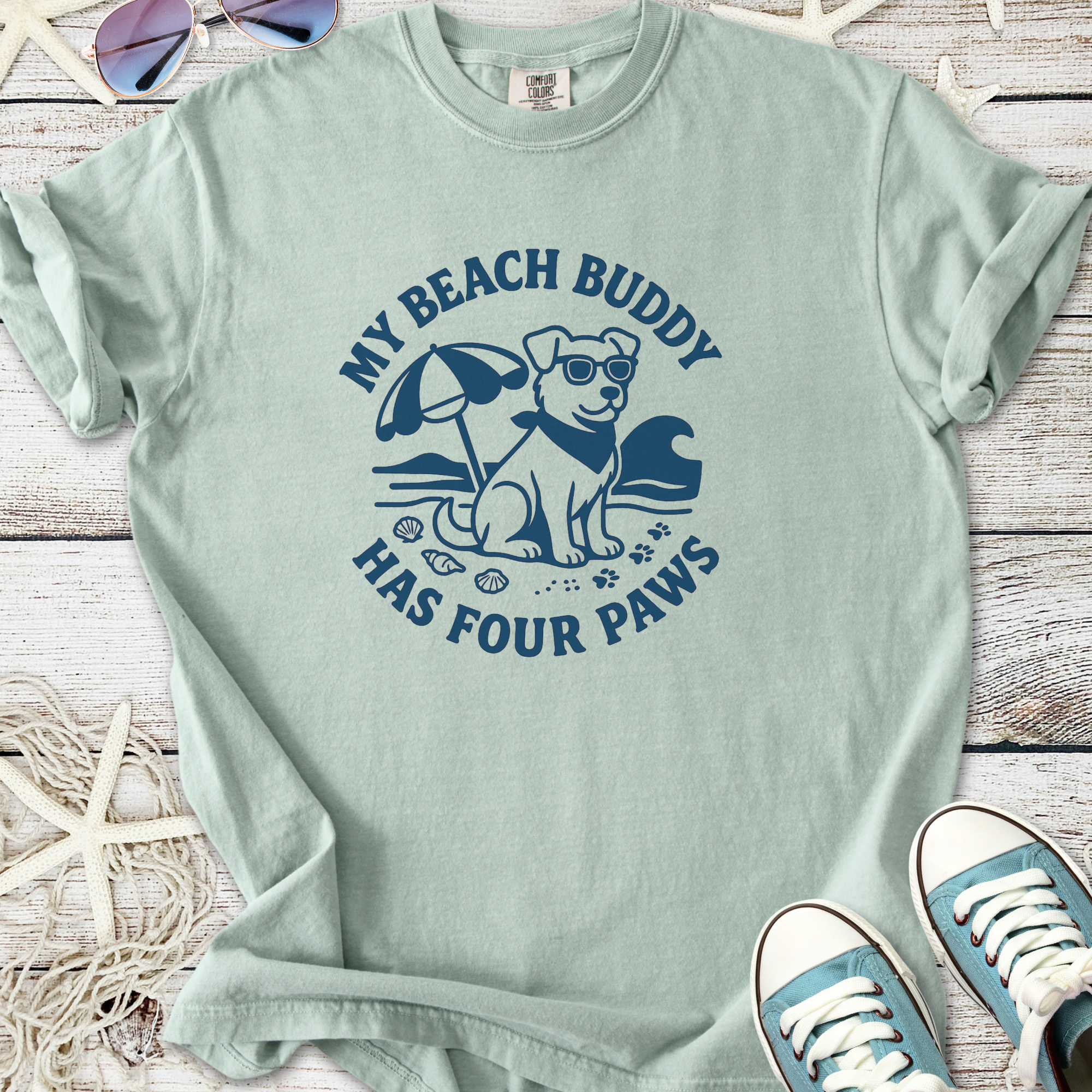 Light blue t-shirt featuring a dog graphic with sunglasses, beach umbrella, and text 'My Beach Buddy Has Four Paws'.