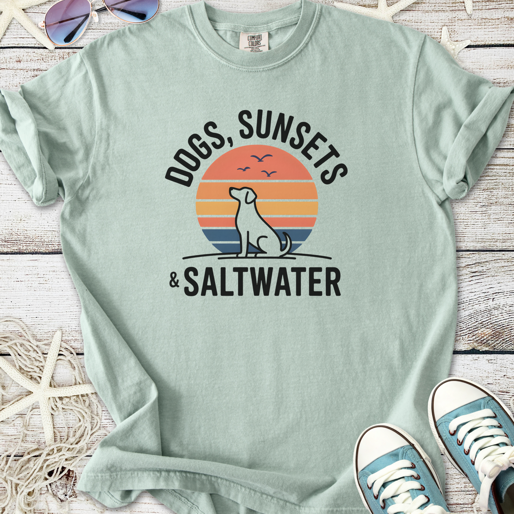Mint green t-shirt with 'Dogs, Sunsets & Saltwater' graphic, cotton material, ideal for beach lovers.