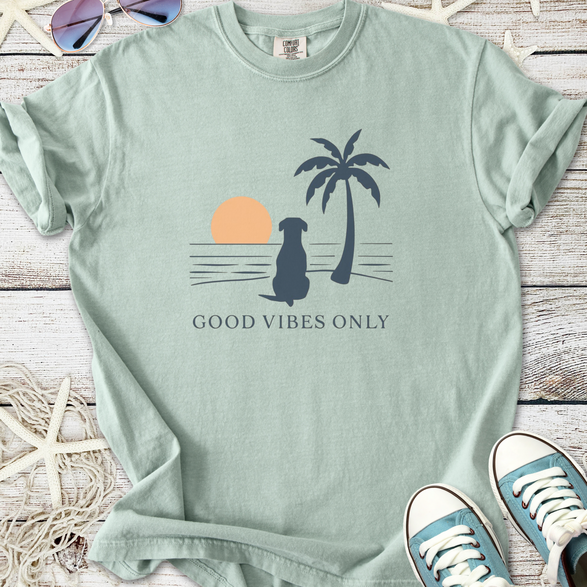 Mint green graphic t-shirt featuring a dog, palm tree, and sunset with the phrase 'Good Vibes Only'.