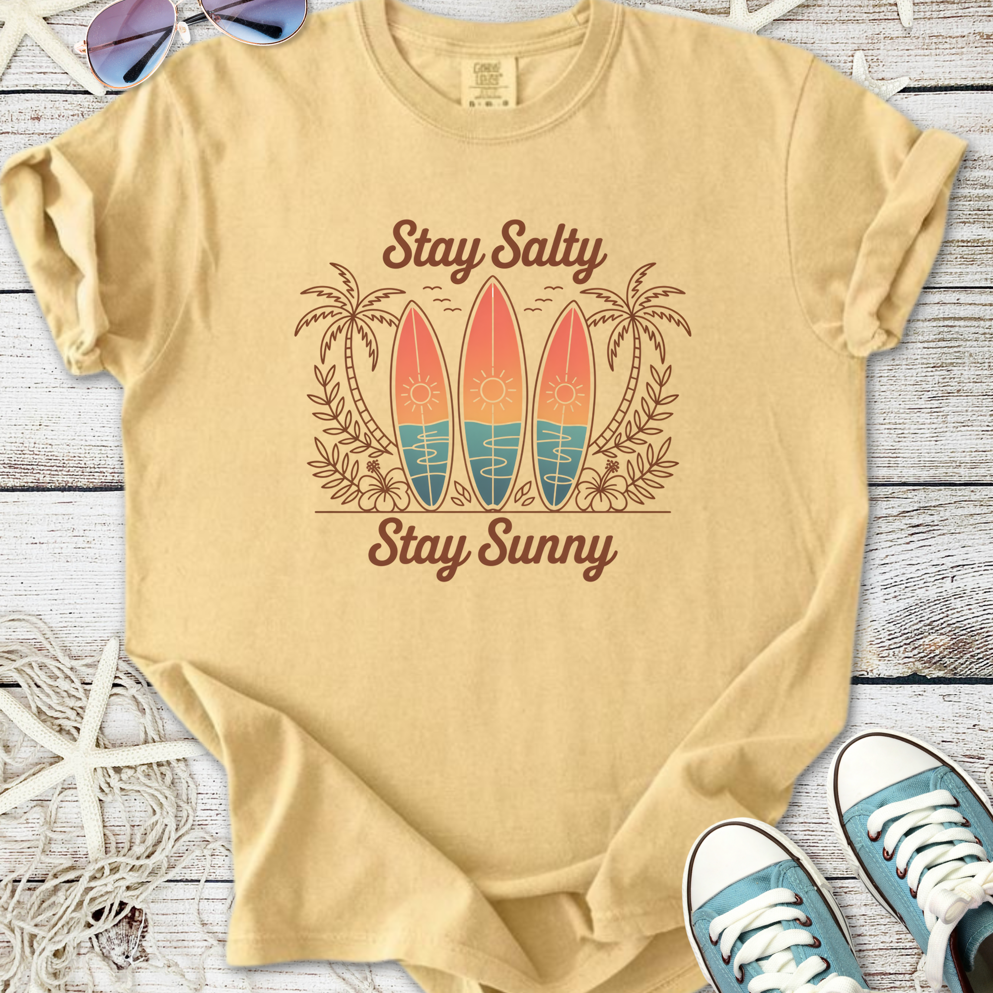 Light beige t-shirt with 'Stay Salty Stay Sunny' surf design, featuring colorful surfboards and beach motifs.