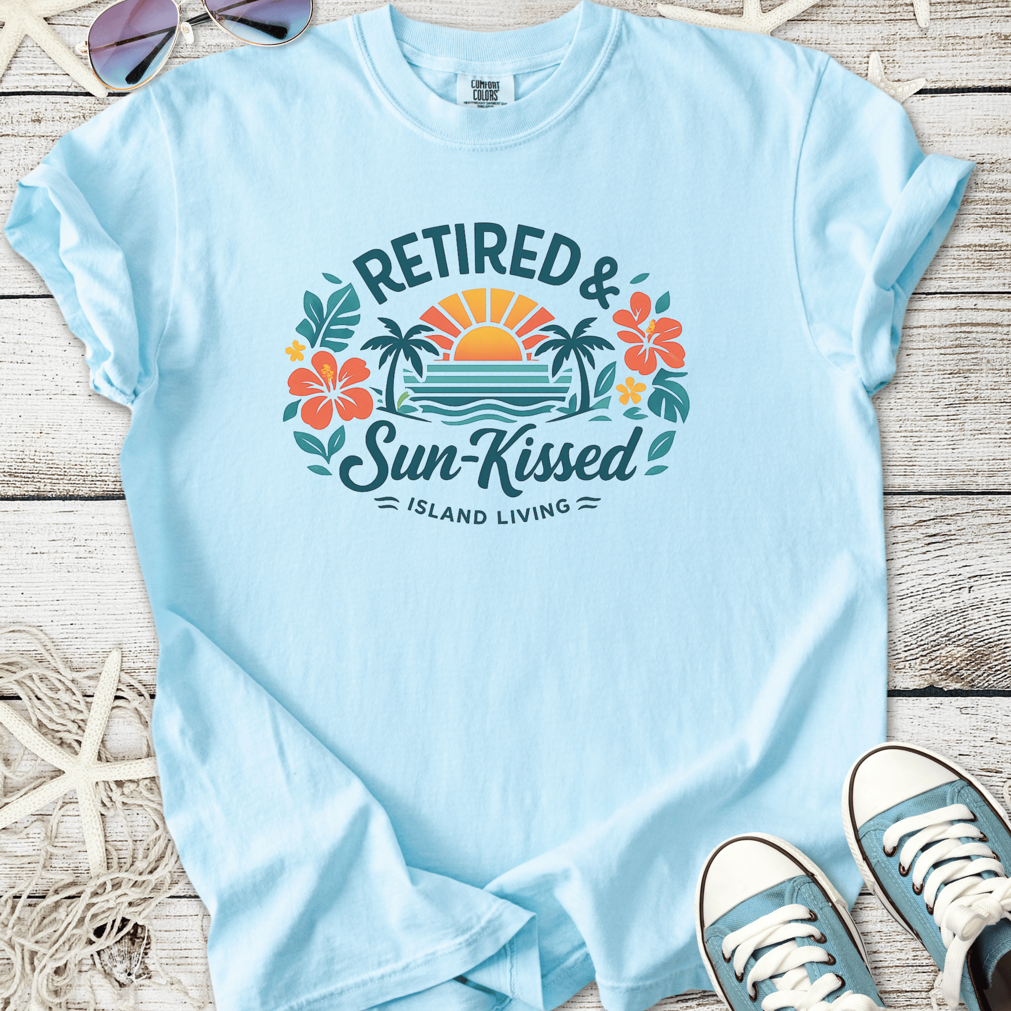Light blue cotton t-shirt with 'Retired & Sun-Kissed' graphic, featuring tropical flowers and a sunset design.
