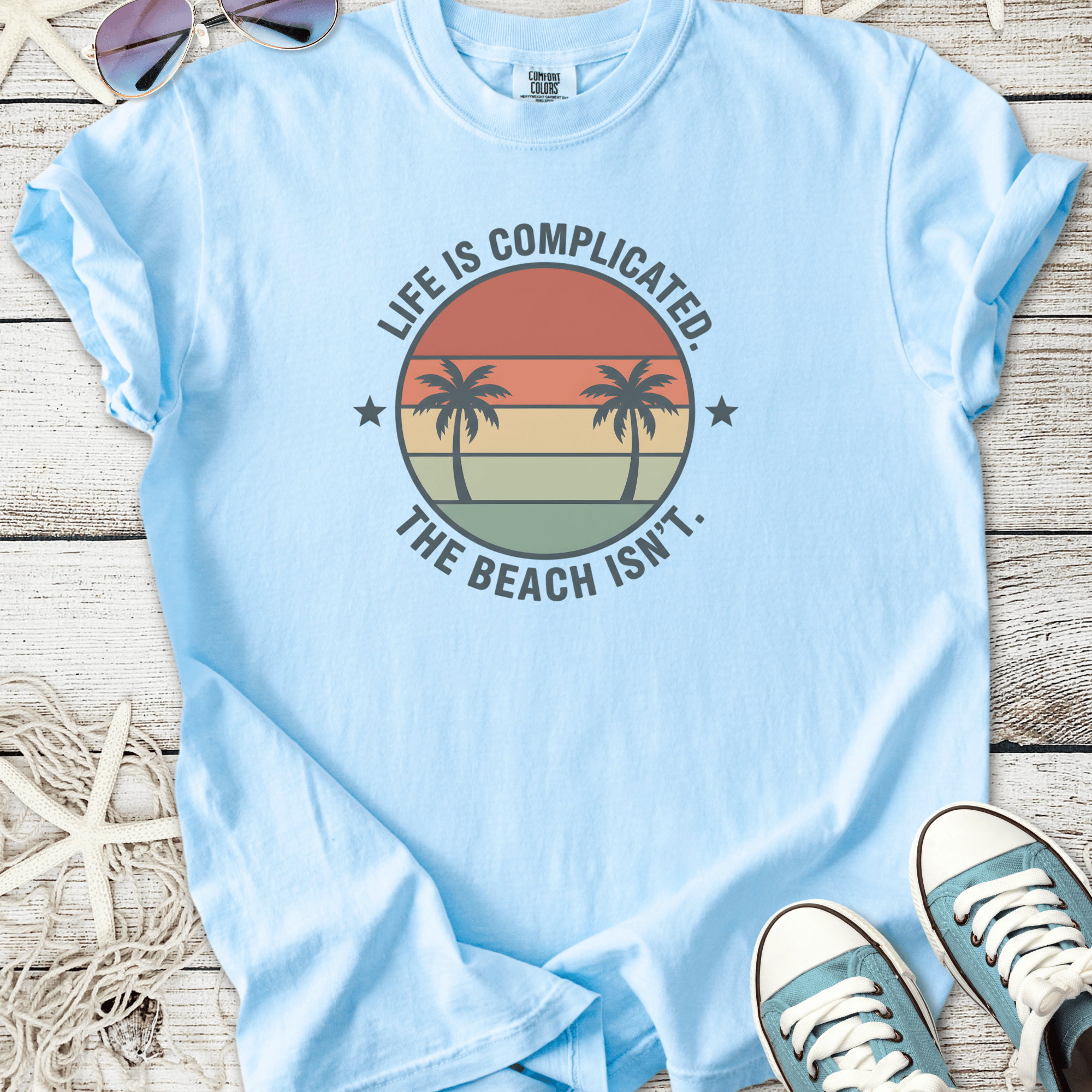 Light blue t-shirt with 'Life is Complicated. The Beach Isn't.' design and palm trees.