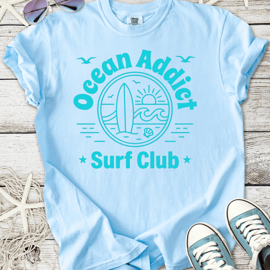Light blue Ocean Addict Surf Club t-shirt featuring surfboard and sun graphic, perfect for beach lovers.
