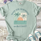 Light seafoam green t-shirt with palm tree graphic and 'Made for Mornings on the Coast' text.