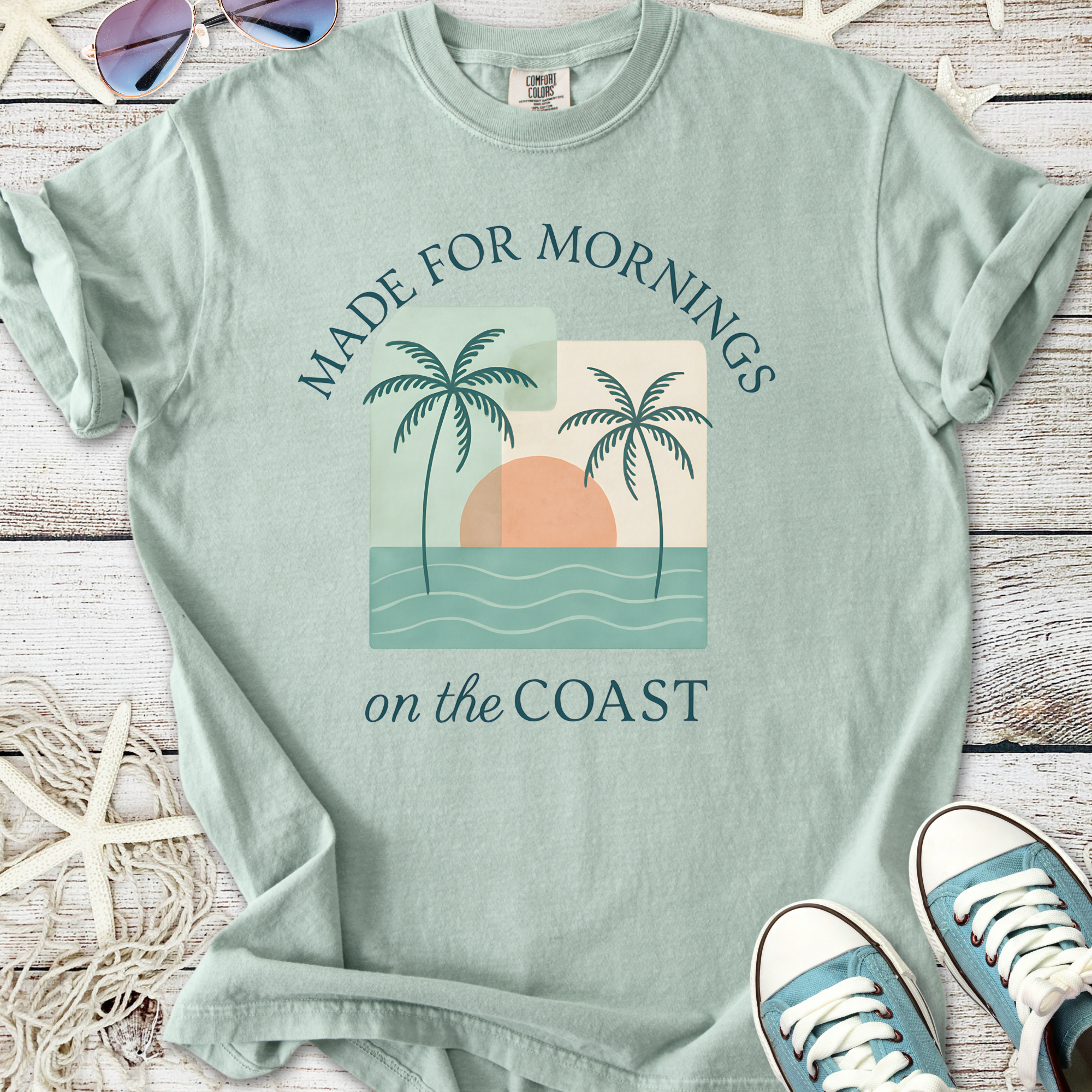 Light seafoam green t-shirt with palm tree graphic and 'Made for Mornings on the Coast' text.