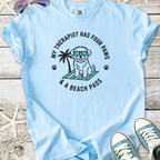 Light blue t-shirt featuring a playful dog graphic with sunglasses and palm tree, perfect for dog lovers.