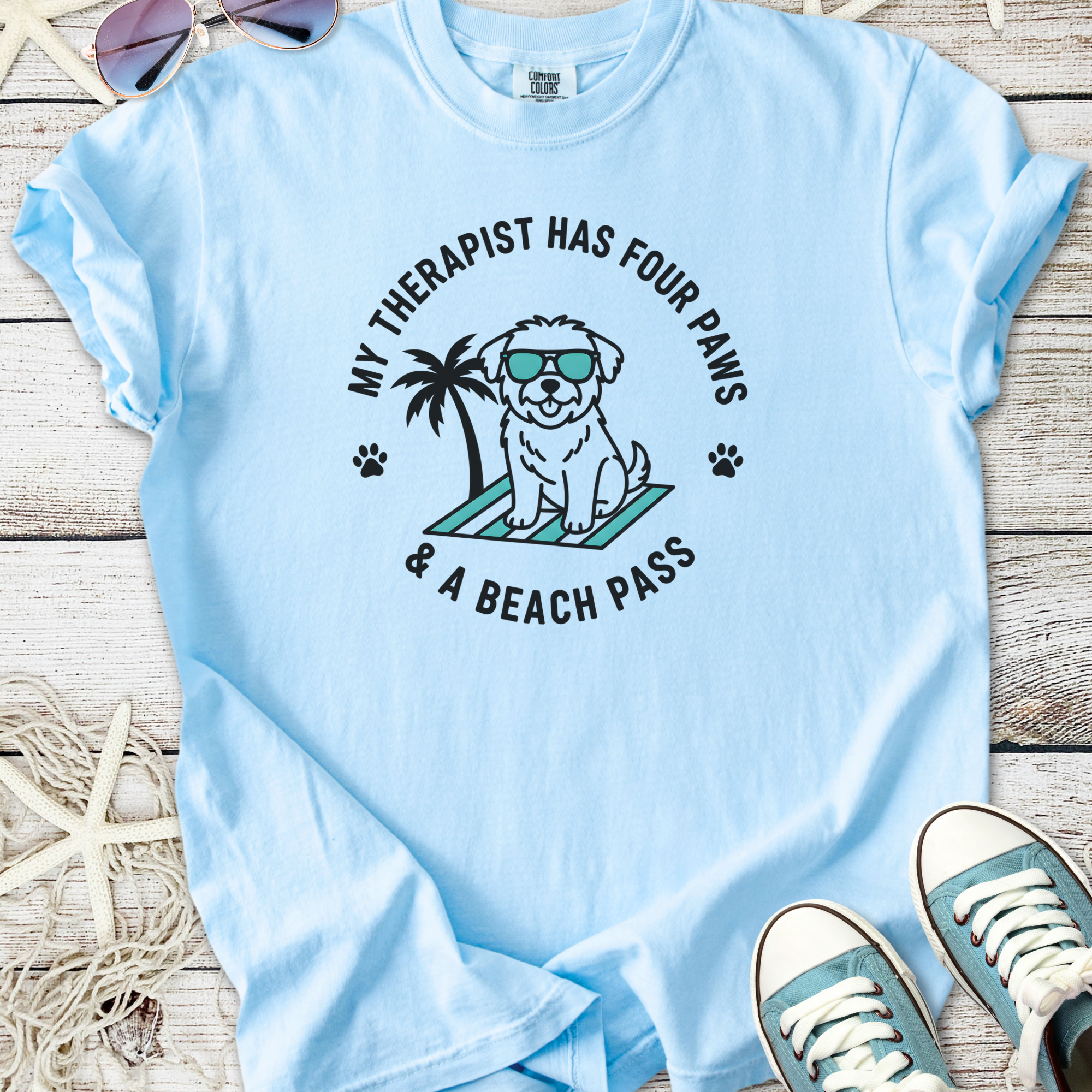Light blue t-shirt featuring a playful dog graphic with sunglasses and palm tree, perfect for dog lovers.
