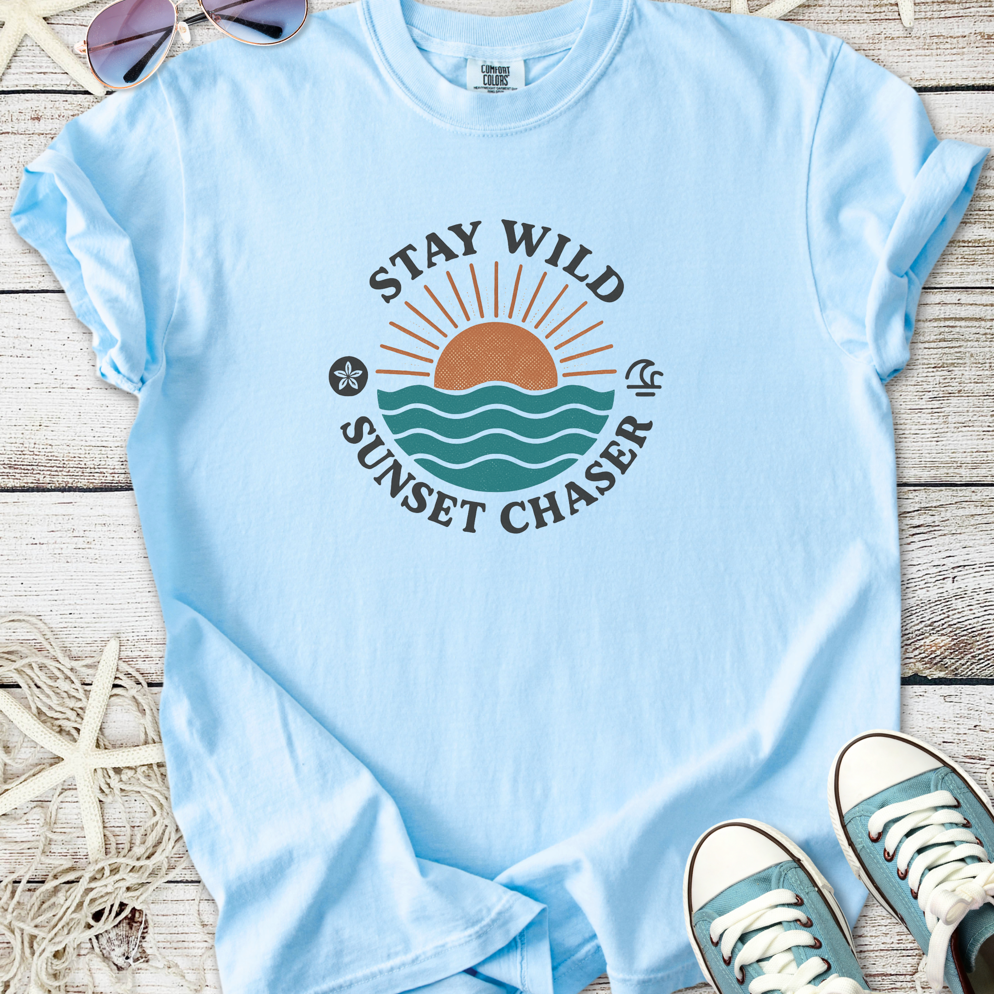 Light blue cotton t-shirt with 'Stay Wild Sunset Chaser' graphic featuring a sunset and waves.