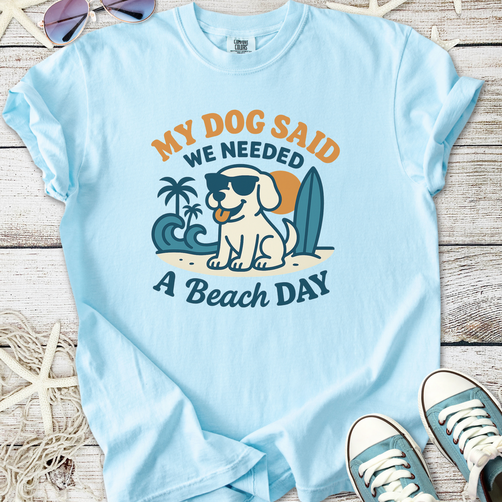 Light blue t-shirt featuring a cartoon dog wearing sunglasses, captioned 'My Dog Said We Needed A Beach Day'.