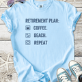 Light blue t-shirt with 'Retirement Plan: Coffee. Beach. Repeat' printed design, ideal for casual wear.