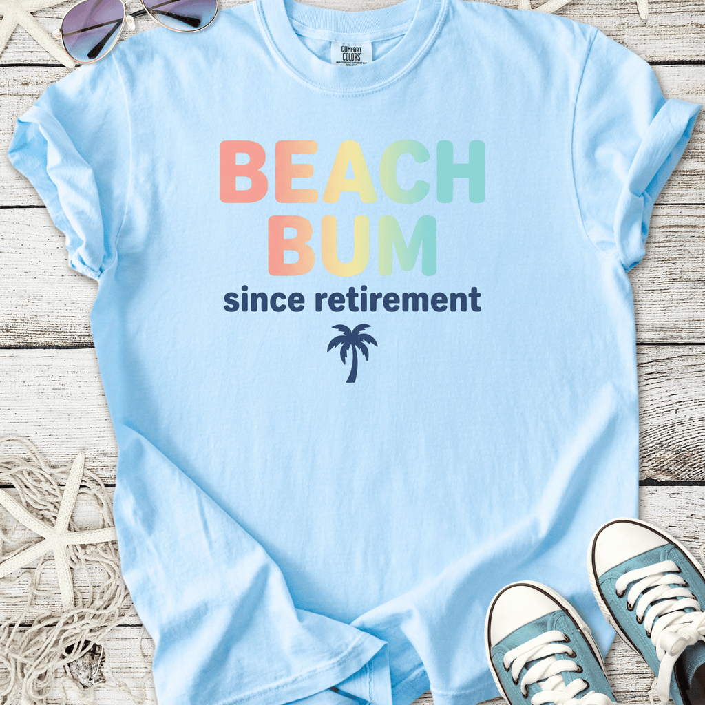 Light blue cotton t-shirt with 'Beach Bum since retirement' graphic and palm tree design.