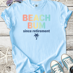 Light blue cotton t-shirt with 'Beach Bum since retirement' graphic and palm tree design.