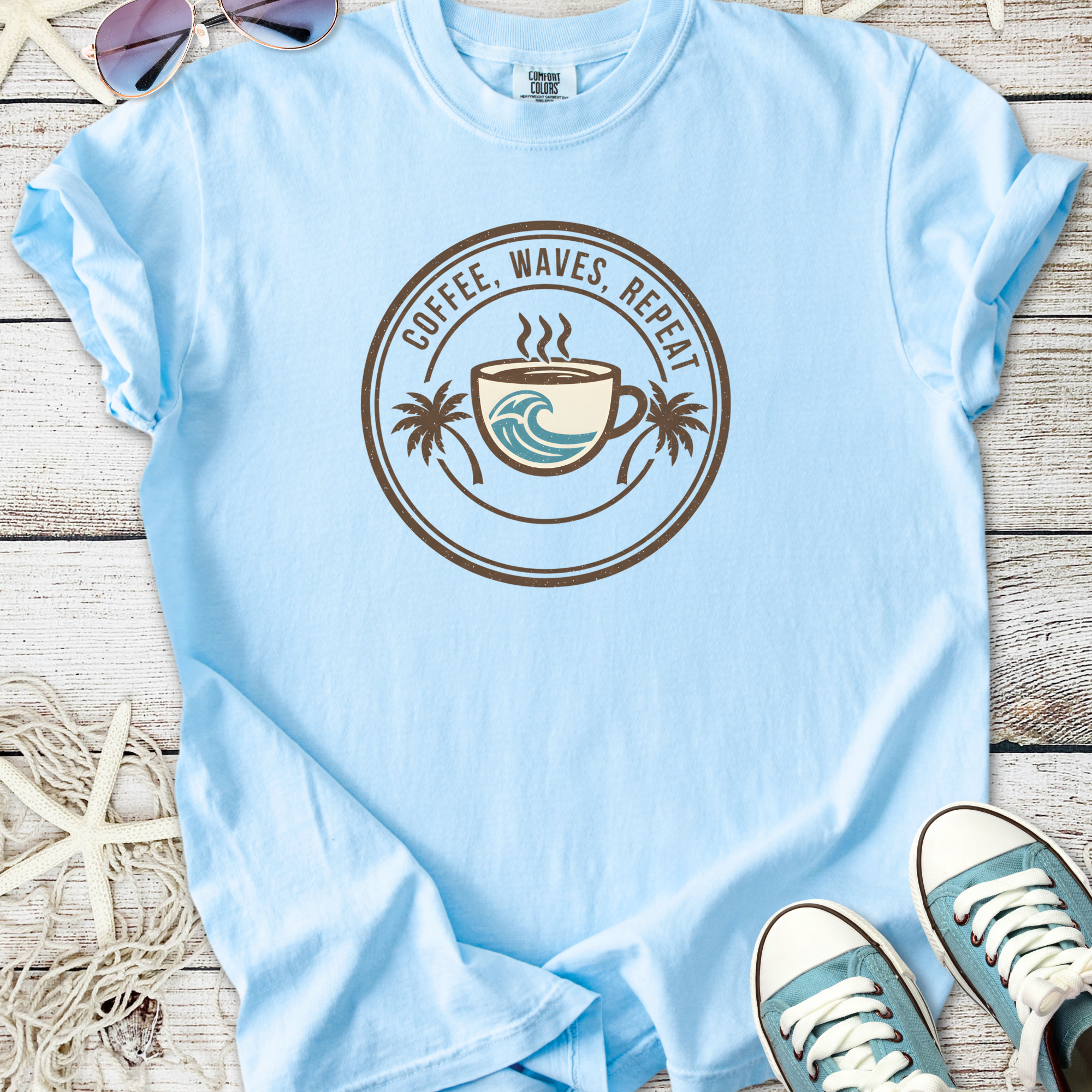 Light blue t-shirt with 'Coffee, Waves, Repeat' graphic and palm trees, perfect for beach lovers.
