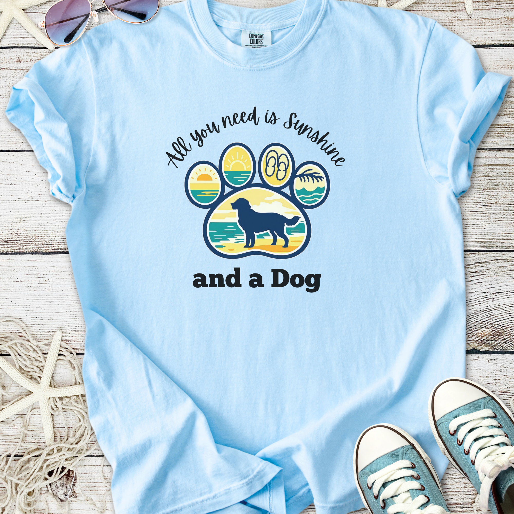 Light blue t-shirt with dog paw graphic and 'All you need is sunshine and a Dog' text, made of soft cotton.