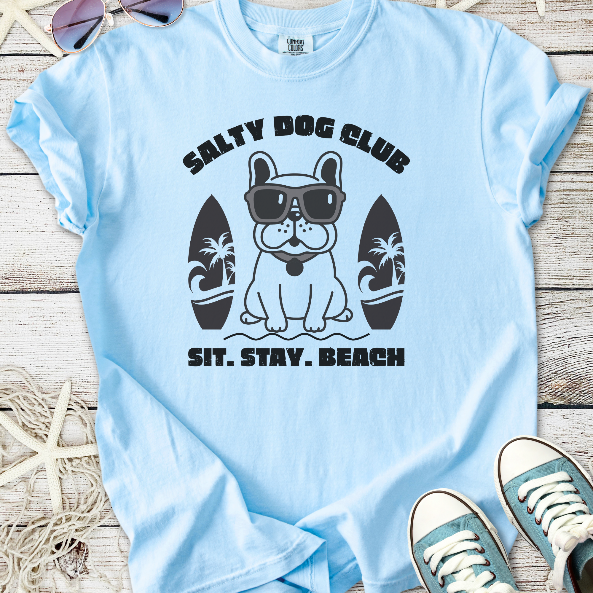 Light blue t-shirt featuring a cool dog graphic with sunglasses and surfboards, perfect for beach lovers.