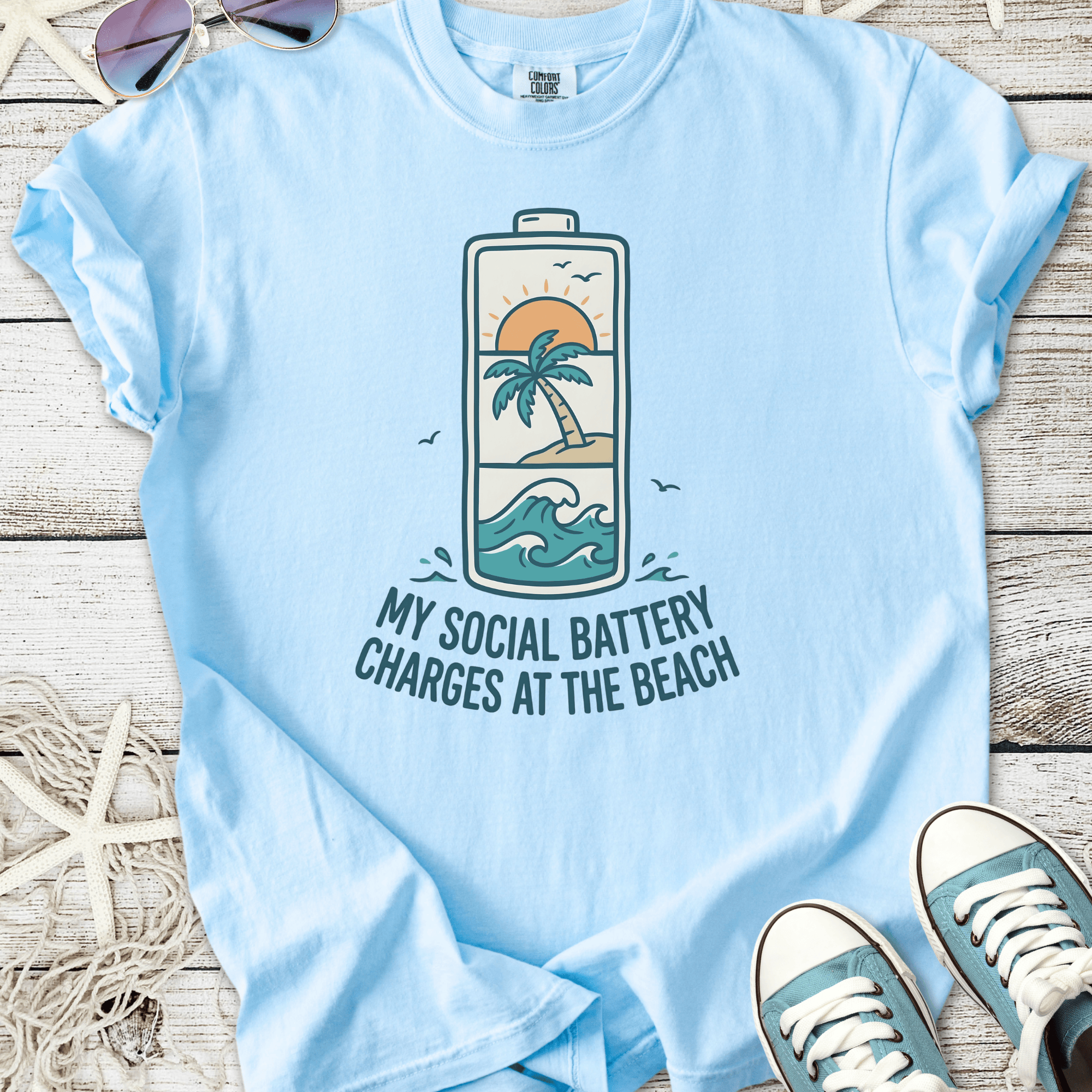 Light blue t-shirt with beach-themed graphic, 'My Social Battery Charges at the Beach' text.