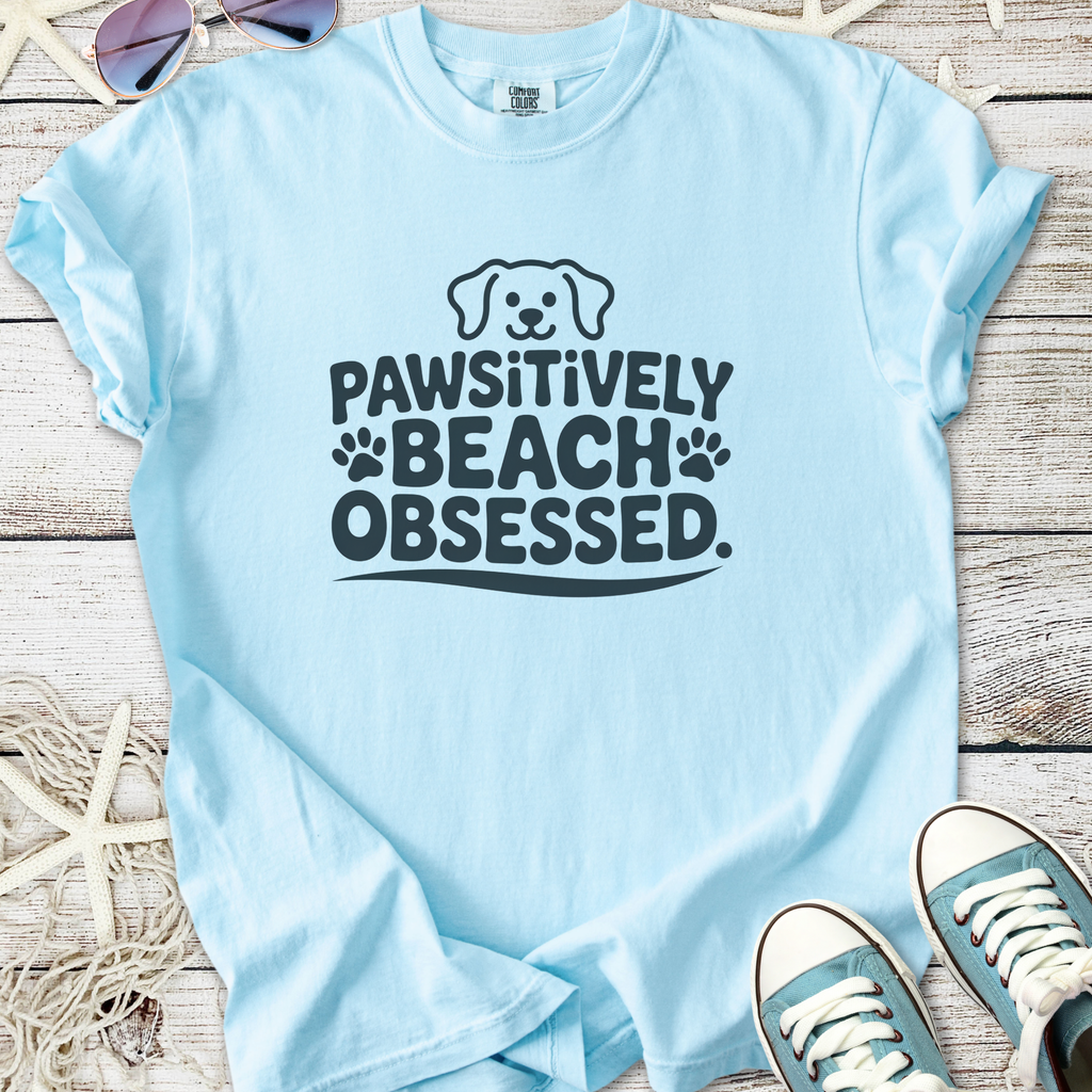 Light blue t-shirt with 'Pawsitively Beach Obsessed' graphic, perfect for dog lovers.