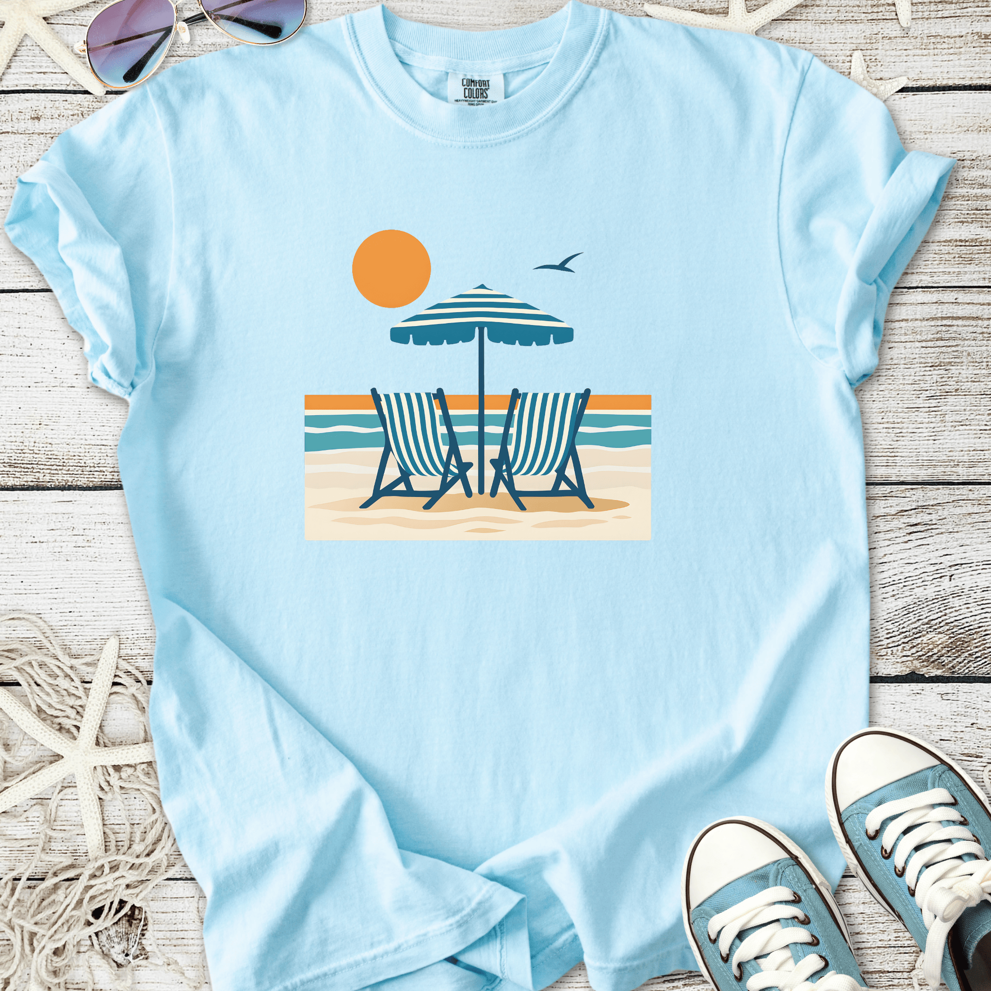 Light blue t-shirt featuring beach chairs, an umbrella, and sun graphic, perfect for summer outings.