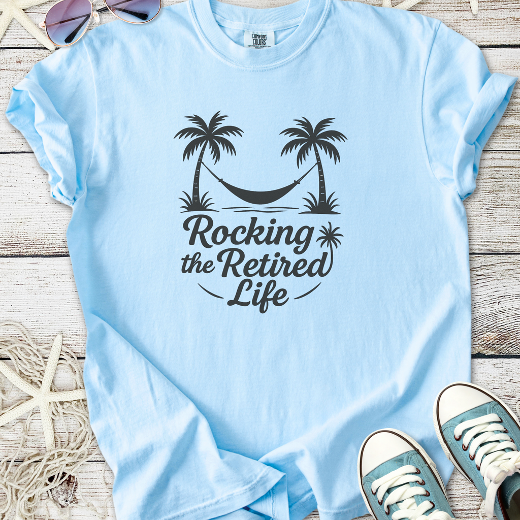 Light blue cotton t-shirt with 'Rocking the Retired Life' graphic featuring palm trees and a hammock.