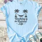 Light blue cotton t-shirt with 'Rocking the Retired Life' graphic featuring palm trees and a hammock.