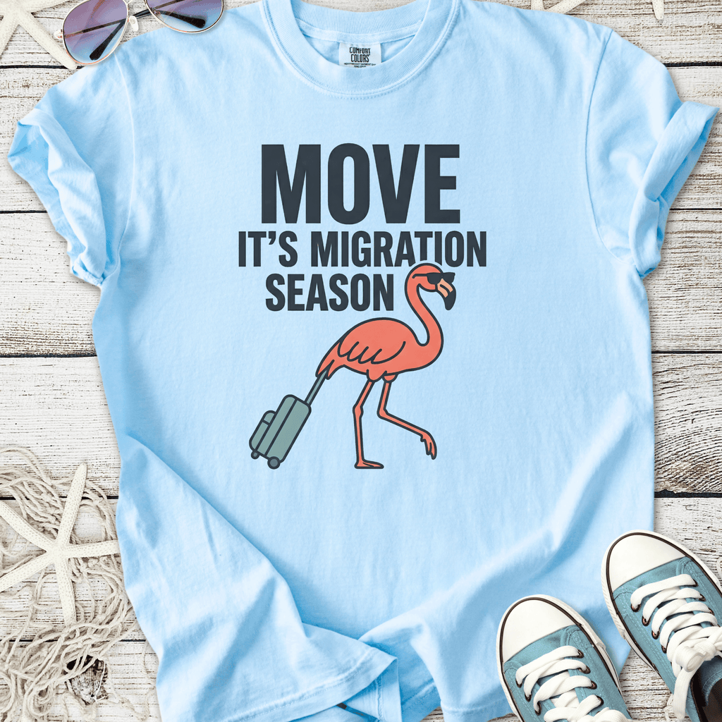 Light blue t-shirt featuring a flamingo with luggage and 'Move It's Migration Season' text.