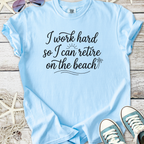 Light blue graphic tee with 'I work hard so I can retire on the beach' text, perfect for beach lovers.