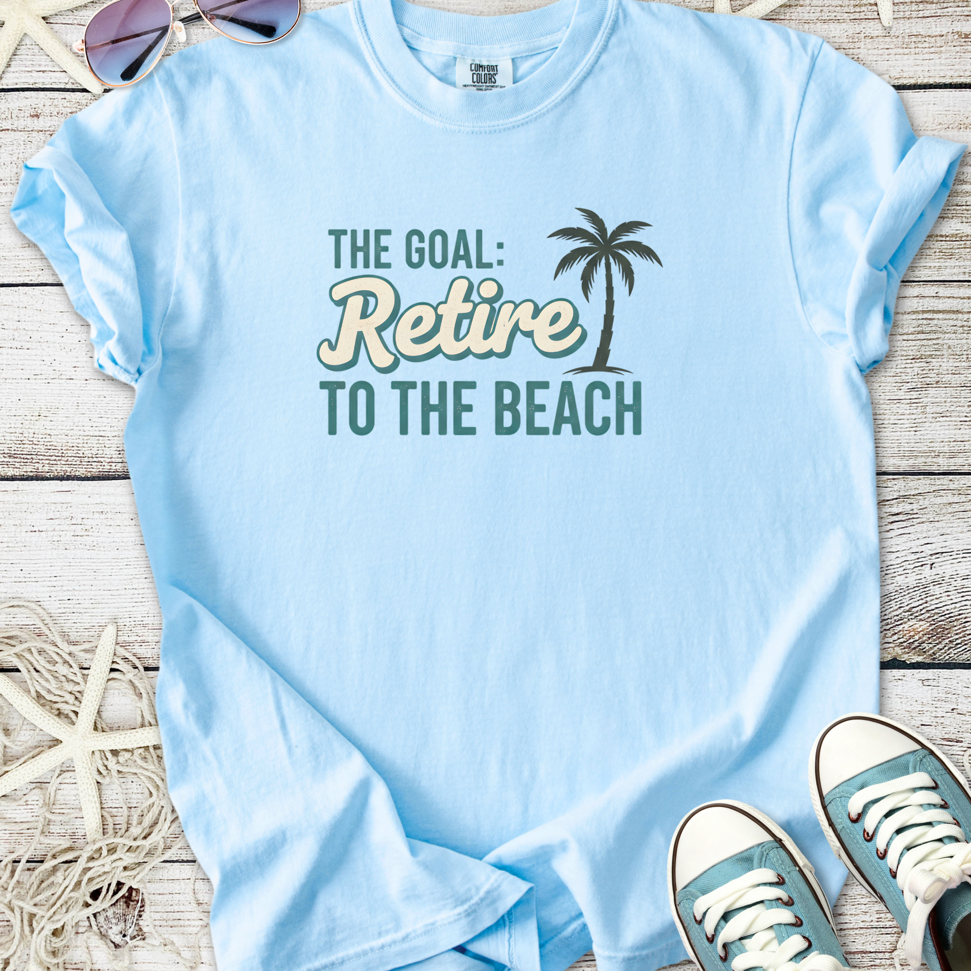 Light blue t-shirt with 'Retire to the Beach' graphic, soft cotton material, perfect for summer wear.