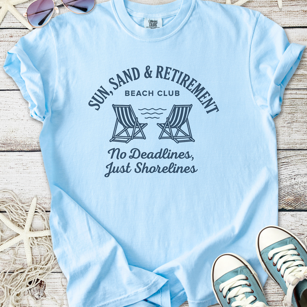 Light blue t-shirt featuring 'Sun, Sand & Retirement Beach Club' graphic. Perfect for relaxed beach days.