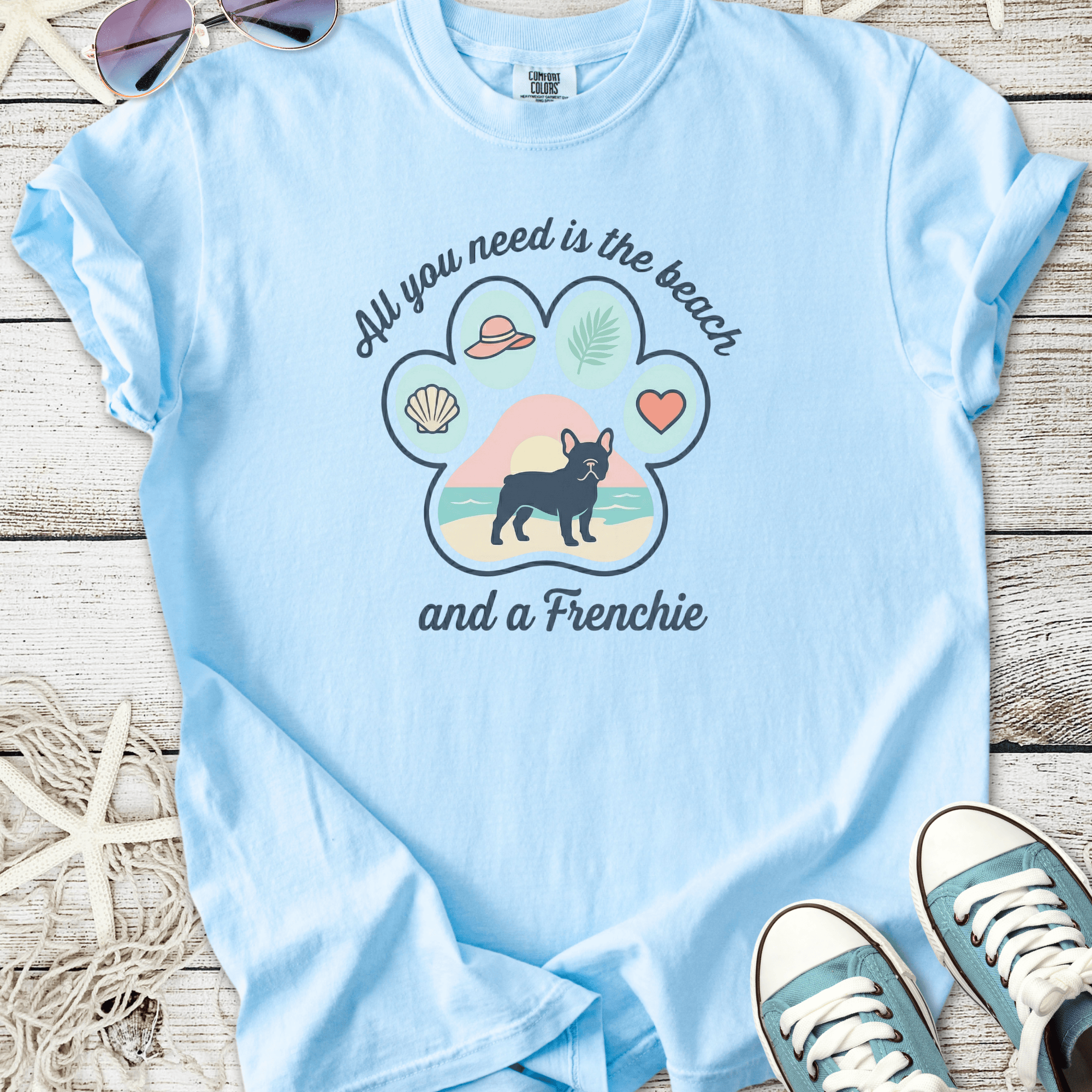 Light blue t-shirt featuring a cute Frenchie graphic with beach themes and the text 'All you need is the beach'.