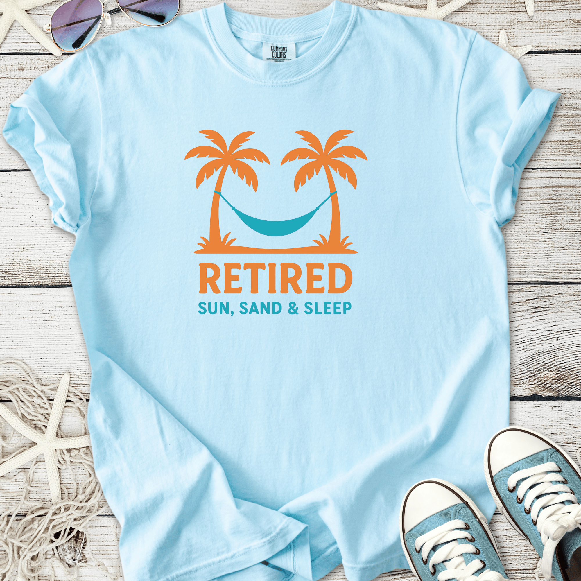 Light blue cotton t-shirt with 'Retired Sun, Sand & Sleep' graphic, featuring palm trees and a hammock.