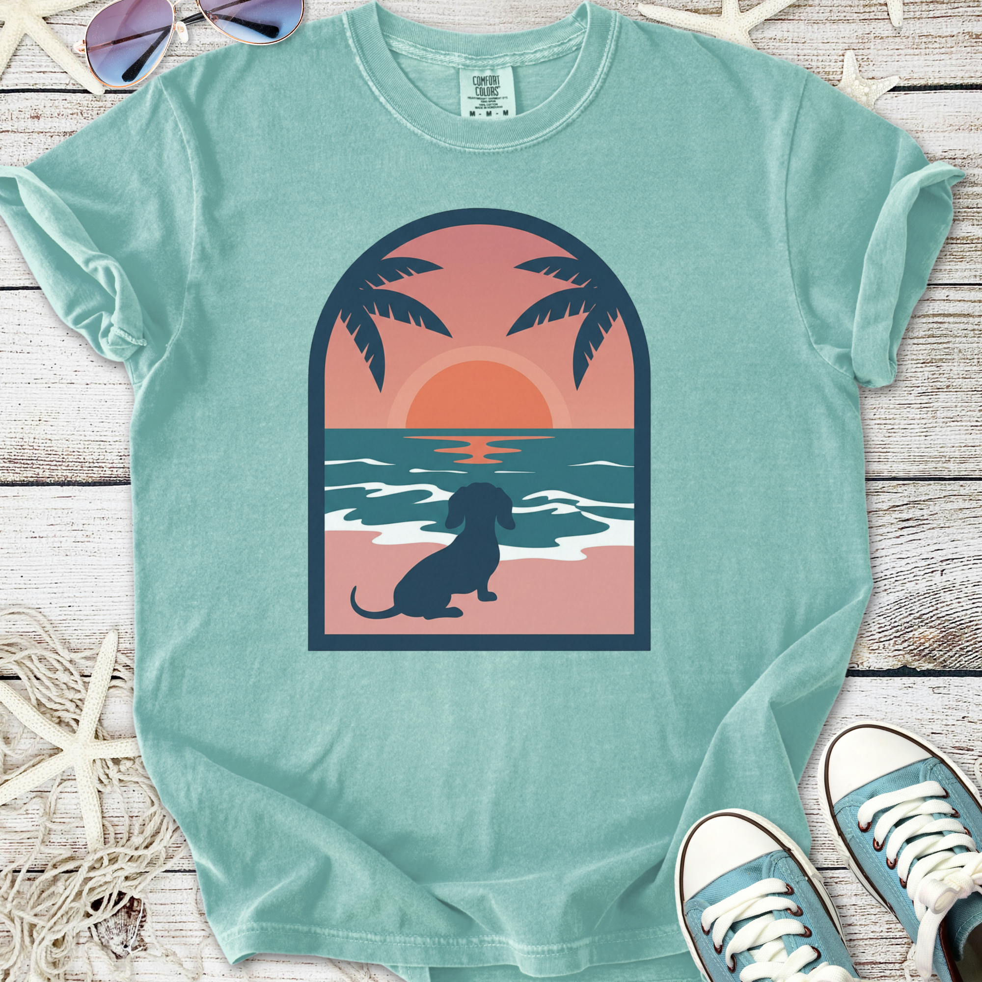 Mint green t-shirt featuring a sunset and dachshund graphic, perfect for dog lovers and beach enthusiasts.