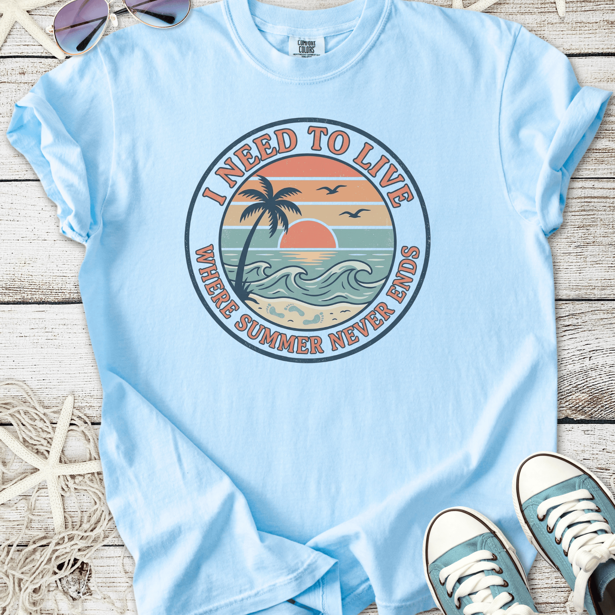Light blue graphic t-shirt featuring a tropical sunset and palm tree design, perfect for summer.