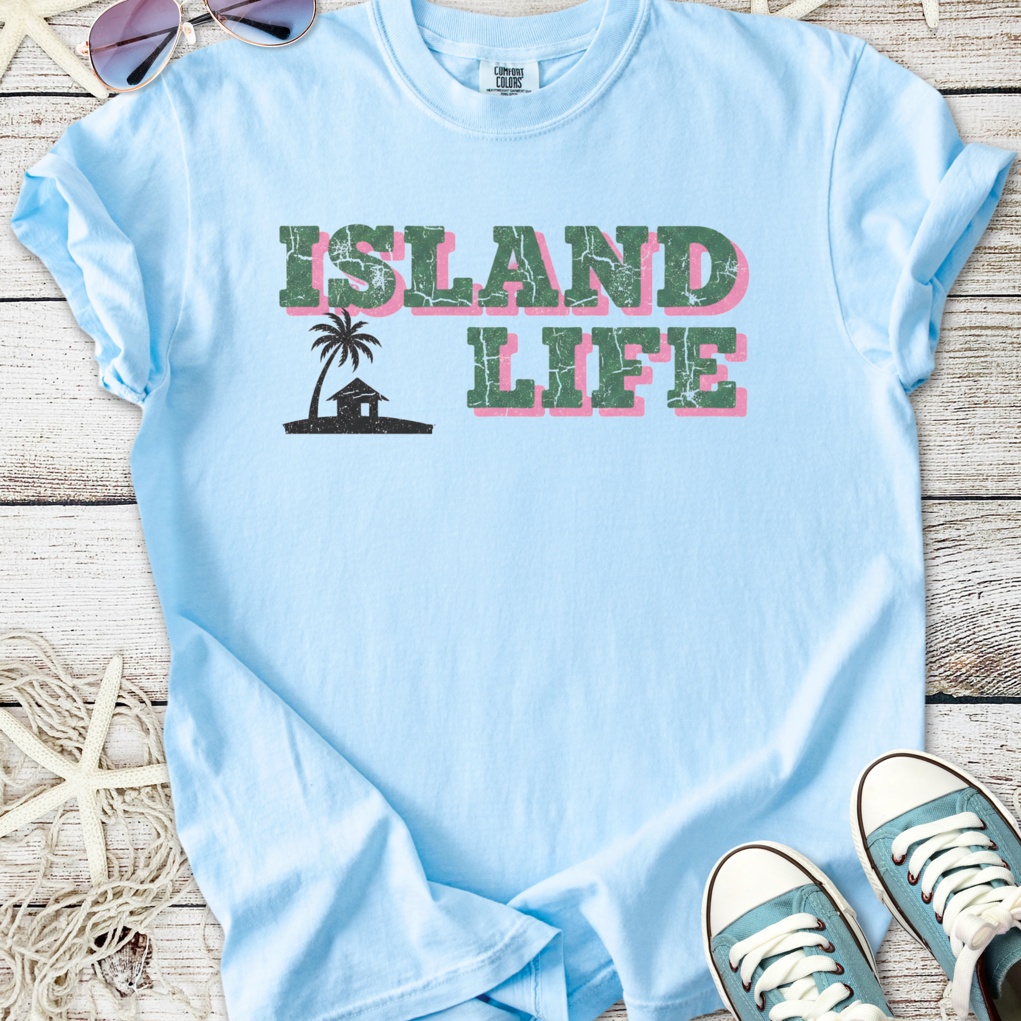 Light blue t-shirt featuring 'Island Life' graphic with palm tree and hut, perfect for casual summer wear.