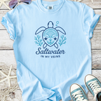 Light blue t-shirt featuring a turtle graphic with 'Saltwater in My Veins' text, made from soft cotton.