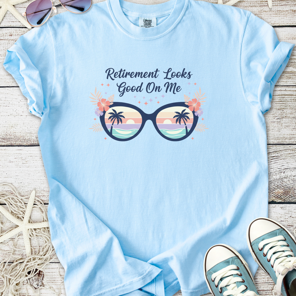 Light blue t-shirt with 'Retirement Looks Good On Me' graphic featuring tropical sunglasses and palm trees.