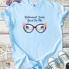 Light blue t-shirt with 'Retirement Looks Good On Me' graphic featuring tropical sunglasses and palm trees.
