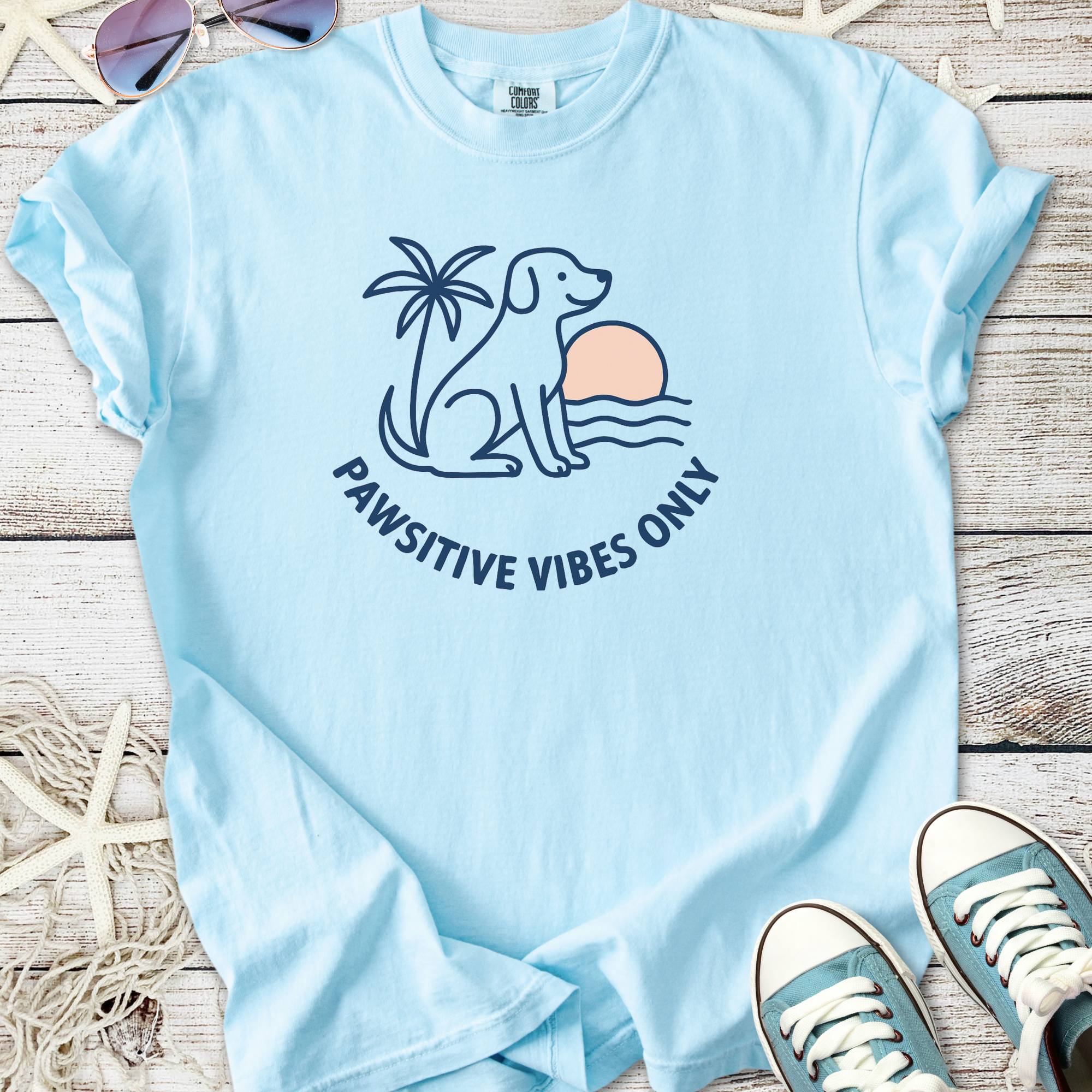 Light blue t-shirt featuring a dog, palm tree, and 'Pawsitive Vibes Only' graphic design.