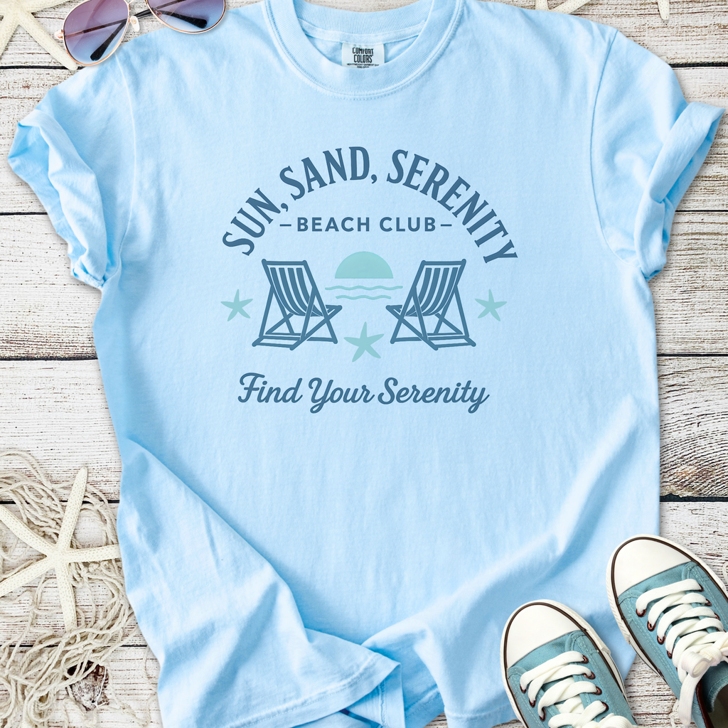 Light blue t-shirt featuring 'Sun Sand Serenity Beach Club' graphic, perfect for beach lovers.