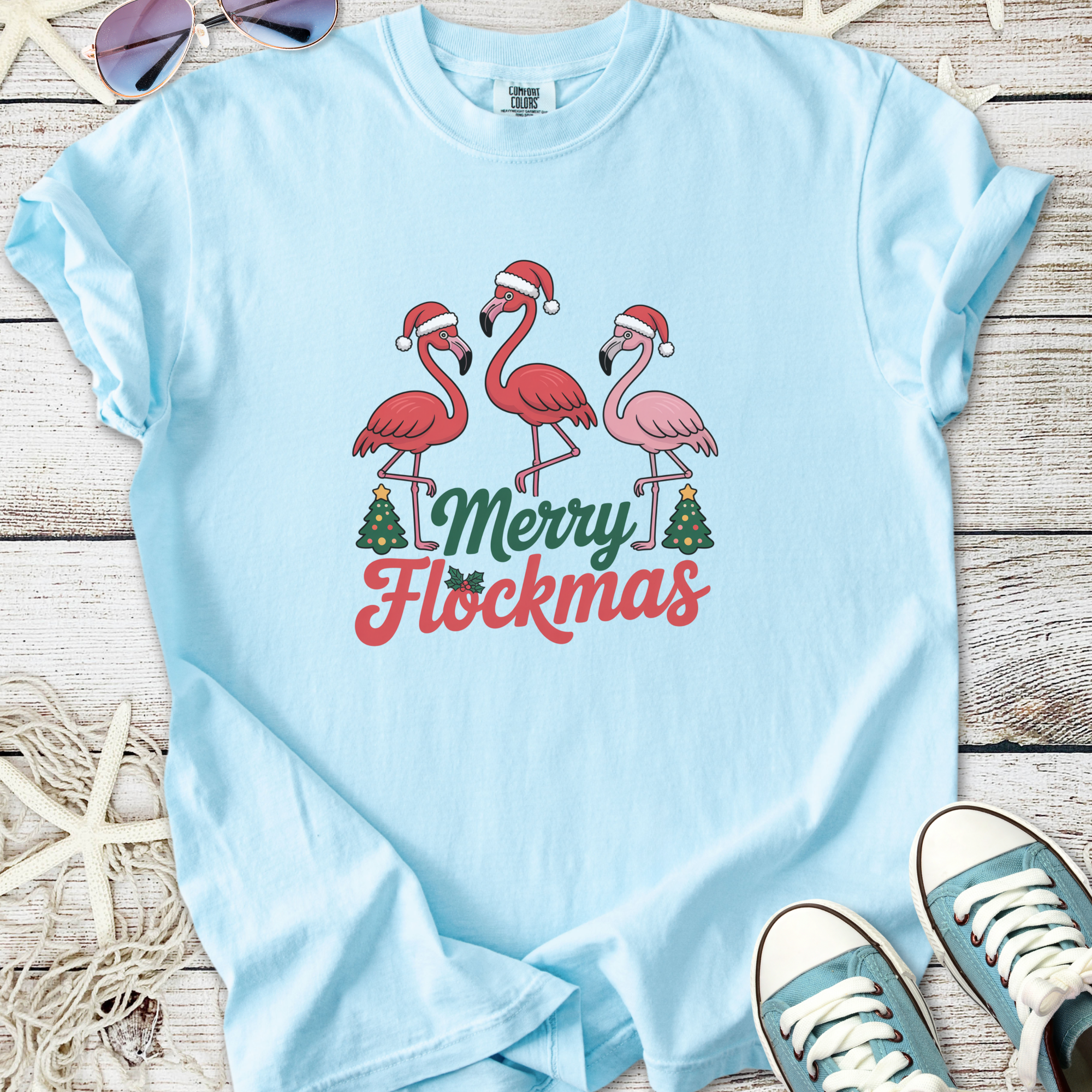 Light blue t-shirt featuring three festive flamingos with Santa hats and 'Merry Flockmas' text.