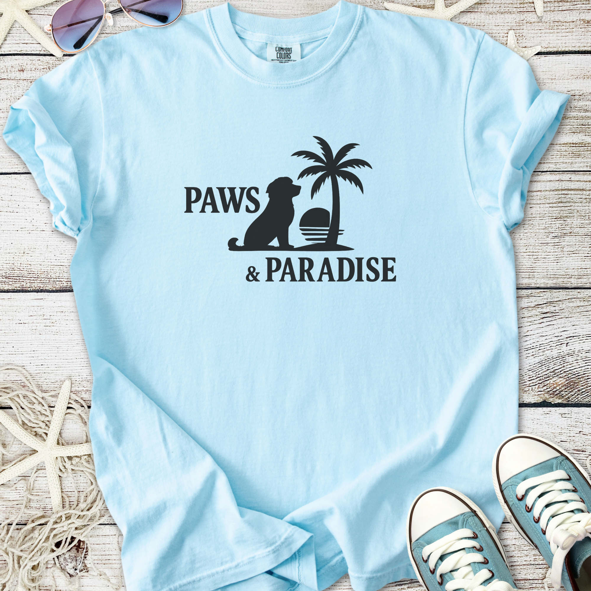 Light blue unisex t-shirt featuring 'Paws & Paradise' graphic with a dog and palm tree design.