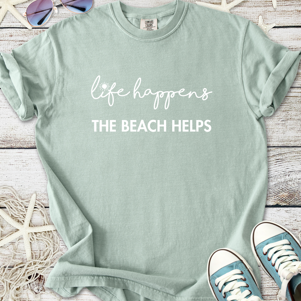 Mint green t-shirt featuring 'life happens, the beach helps' in stylish lettering, perfect for beach lovers.