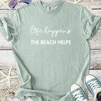 Mint green t-shirt featuring 'life happens, the beach helps' in stylish lettering, perfect for beach lovers.