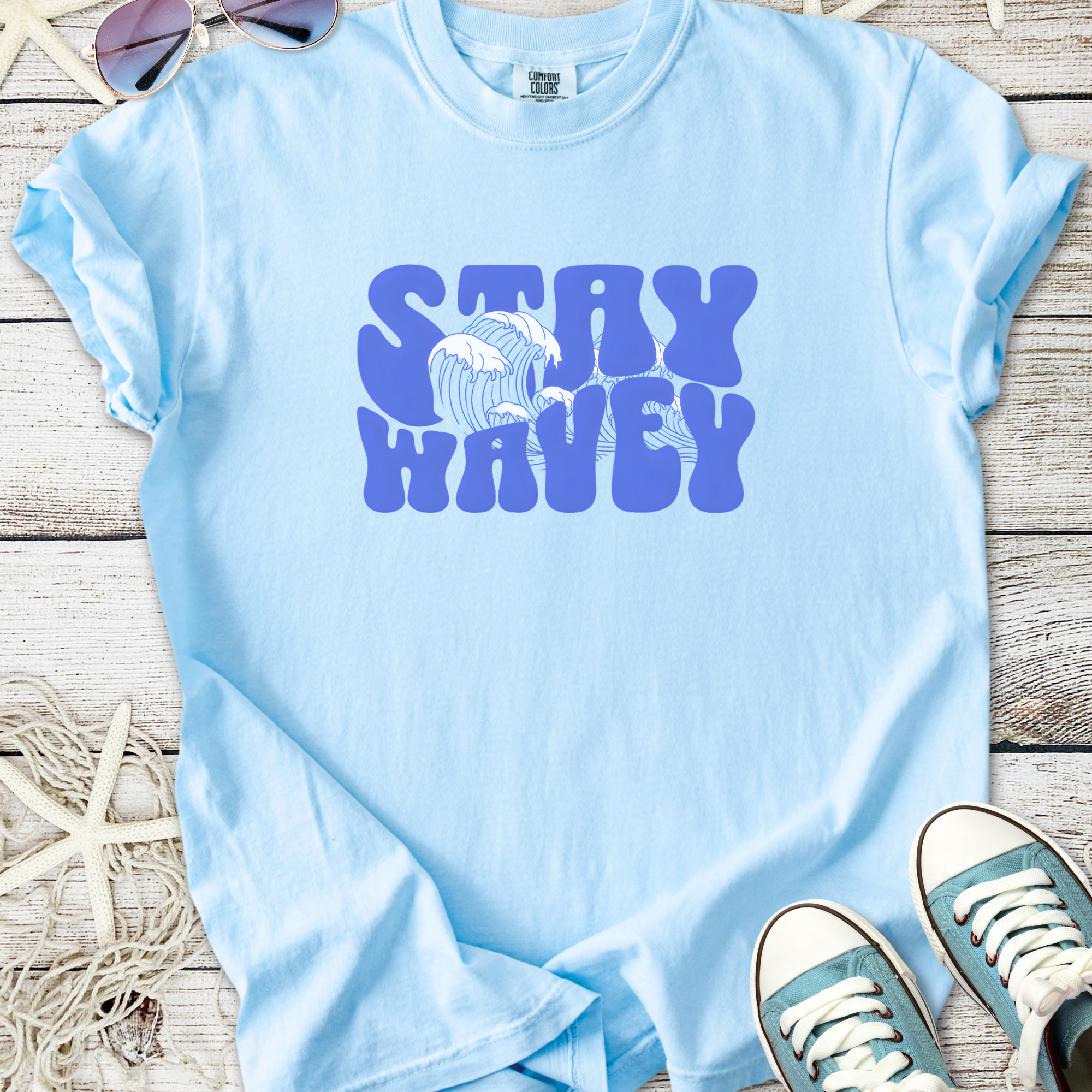 Light blue cotton t-shirt with 'Stay Wavey' graphic and wave design, perfect for beachwear.