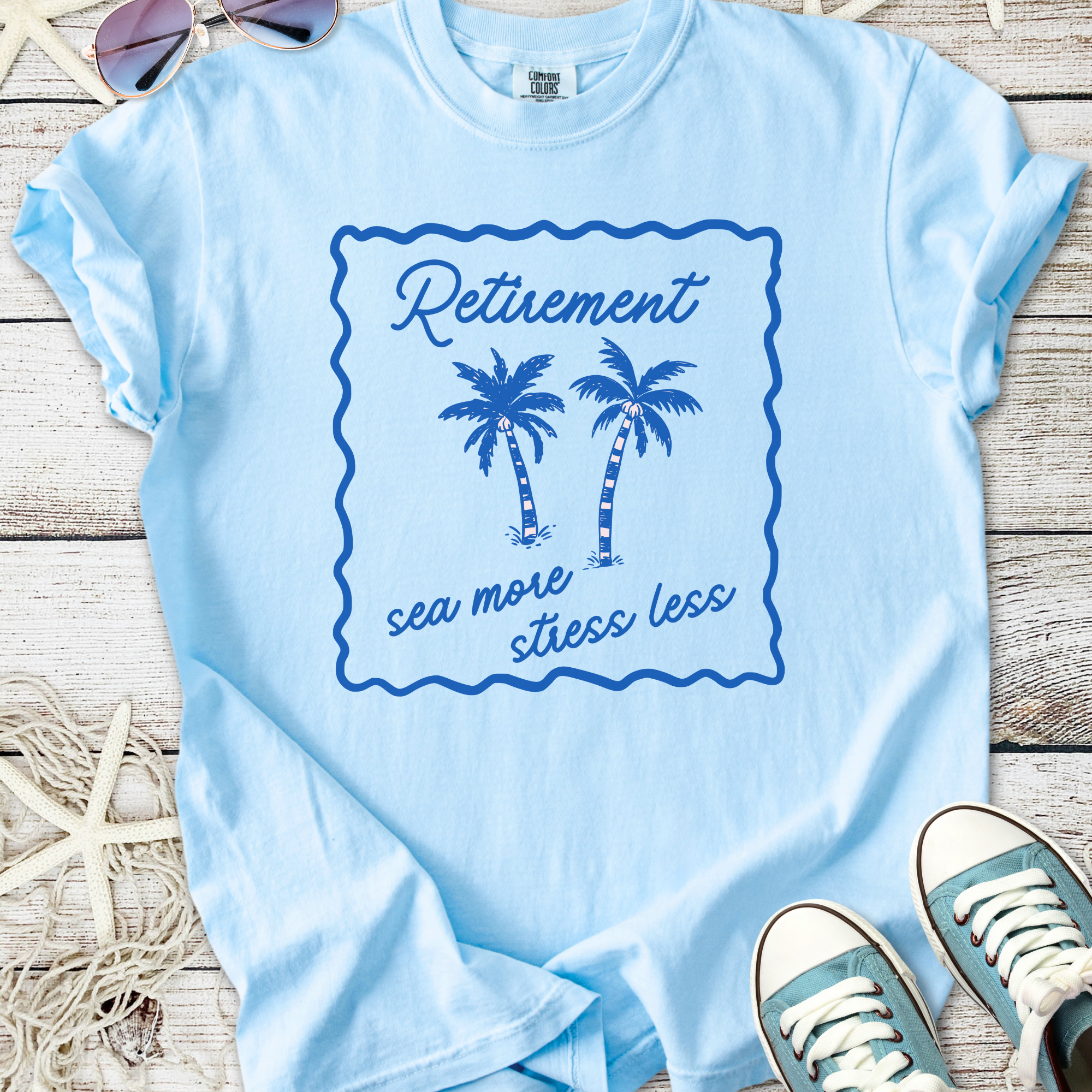 Light blue t-shirt with palm tree graphic and 'Retirement sea more stress less' slogan.