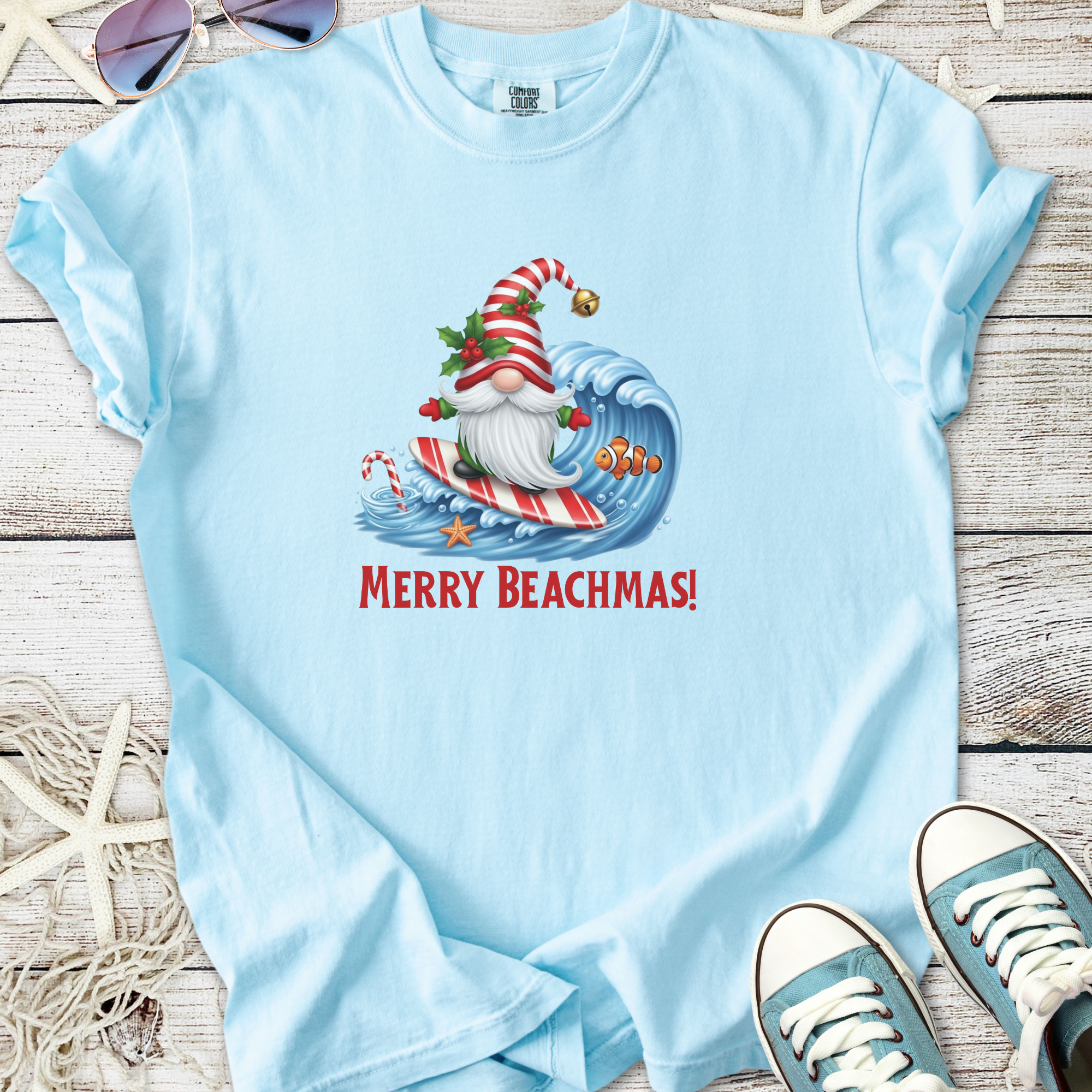 Light blue t-shirt featuring a surfing Santa with 'Merry Beachmas!' slogan, perfect for festive beach outings.