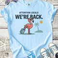 Light blue cotton t-shirt with a flamingo graphic and text 'WE'RE BACK.' for a fun beach vibe.