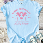 Light blue t-shirt featuring 'Sunset Social Club' print with palm trees, perfect for beach lovers.